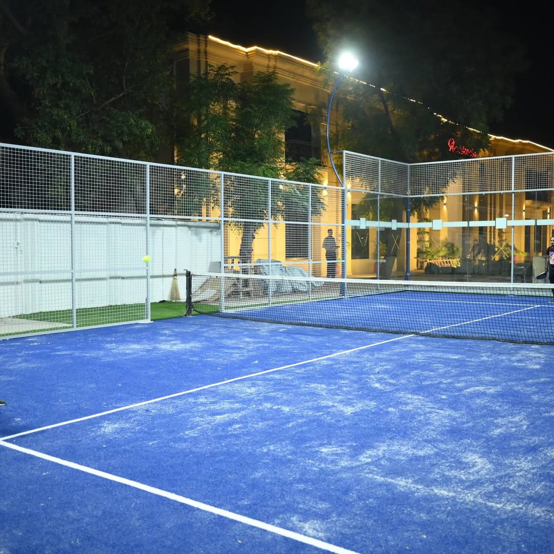 The glass-walled padel court beside the clubhouse at night