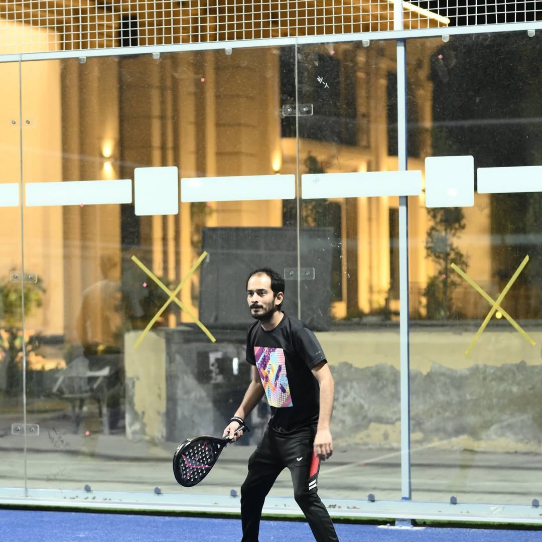 Member serving on the floodlit padel court at night